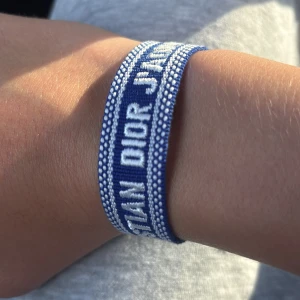 Blått Christian Dior J'Adior armband - Snyggt blått armband från Christian Dior med texten 'J'Adior' broderad i vitt. Armbandet är gjort i tyg med justerbar knytning och tofsar i ändarna. Perfekt accessoar för att lyfta din outfit med en lyxig touch. Kontakta mig vid frågor!🤝 Har 10 stycken armband🔥
