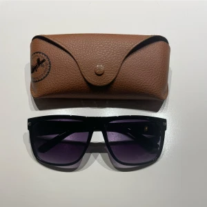 Svarta solglasögon med lila tonade glas - Snygga svarta solglasögon. Bredd framtill 144 mm, skalmlängd 140 mm, höjd 48 mm. OBS! Fodral ingår ej.