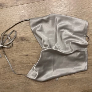 Silvrig satintopp med knytband - Snygg silvrig tubtopp i satin med smala knytband som ger en trendig look. Toppen har en glansig finish och bandeau-modell som sitter snyggt på kroppen. Perfekt för dig som vill sticka ut med en stilren och modern vibe. Storlek S