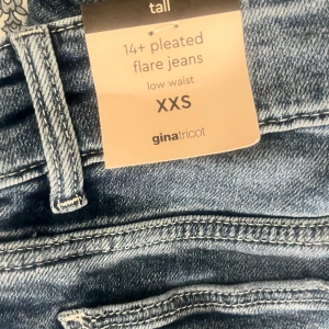 Blå flare jeans från Gina Tricot XXS - Snygga blå flare jeans från Gina Tricot i modellen 14+ pleated flare. Låg midja, bootcut och slitna detaljer vid knäna. Stora fickor fram och dubbla knappar i midjan.