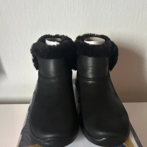 Svarta boots on the go joy med päls - Svarta boots från Skechers Go Walk med mjuk päls runt skaftet och grov sula. Skorna är i hög kvalitet material och har en rund tå. Perfekta för kyliga dagar och riktigt sköna att gå i.
