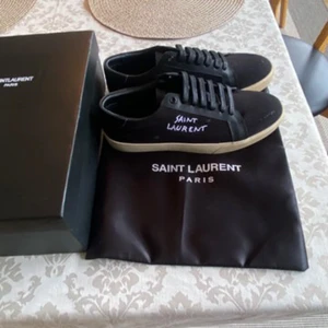 Svarta Saint Laurent sneakers - Snygga svarta sneakers från Saint Laurent med vit logga på sidan och kontrasterande vit sula. svarta skosnören och detaljer i skinn. Perfekta för dig som gillar stilrena och exklusiva sneakers. OBS endast testade, priset är diskuterbart