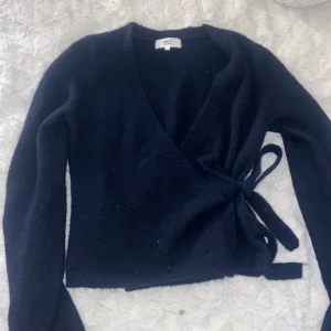 Stickad tröja  - Mysig mörkblå omlottkofta från Gina Tricot i ullblandning. Koftan har långa ärmar, knytband i sidan och en snygg v-ringning! 