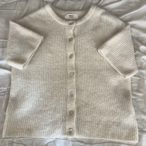 Beige kofta i ullmix från Gina Tricot - Supermysig beige kofta från Gina Tricot i ullblandning. Koftan har ribbstickad struktur, rund halsringning och knappar framtill. Perfekt för lager-på-lager och chill höst- och vinterstil. Knappen längs ner är tyvärr söndrig men finns reserv knapp tillgänglig.