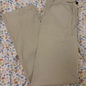 Beiga wide byxor från LXA, strl 38 - Snygga beiga byxor från LXA i storlek 38. De har breda ben, resår i midjan med snörning och två bakfickor. Perfekta för en chill och avslappnad look. Tillverkade i mjukt bomullsmaterial för extra komfort.