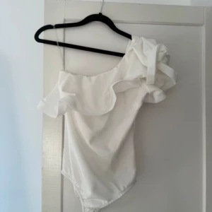 Vit oneshoulder volang body  - Superfin vit body med oneshoulder och volangdetalj. Fick av en kompis för hon använde aldrig den längre och jag har själv inte haft nått tillfälle till att använda den
