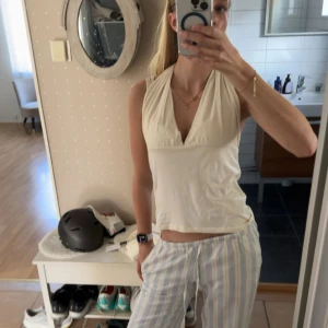 Vit omlott-linnetopp med v-ringning - Säljer en gräddvit/ljusgul ärmlös linne-topp med djup v-ringning och omlott-detalj framtill. Toppen har en croppad passform och är perfekt för varma dagar. Enkel och stilren design som passar till många olika outfits. Toppen är öppen i ryggen och knyts med band på nacken. Aldrig använt, utan endast tvättad. Pris kan dissekeras