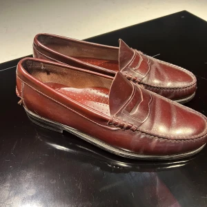 Klassiska bruna loafers i skinn - Snygga loafers i mörkbrunt skinn med klassisk penny loafer-design. Skorna har rund tå, platt sula och fina sömdetaljer längs kanterna. Perfekta för en stilren och tidlös look.