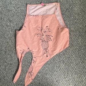 Rosa linnetopp med ananasmönster - Säljer en rosa linnetopp med svart ananasmönster. Toppen har asymmetrisk nederkant och knytband framtill, vilket ger en cool och unik look. Perfekt för varma dagar och somriga vibes. Lätt och luftig i materialet.
