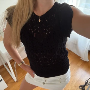 Svart stickad topp från Lindex - Säljer en svart stickad topp från Lindex i storlek S. Toppen är ärmlös med ett snyggt hålmönster och ribbad nederkant. Perfekt att styla med kjol eller jeans för en trendig look. Superfin till både lager-på-lager och som den är!