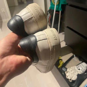 Vita sneakers från Axel Arigato - Snygga vita sneakers från Arigato med svart häl och klassisk snörning. Skorna är i skinn och har en platt sula samt rund tå. Perfekta för en clean och stilren look till vardags. Diskret Arigato-logga bak på sulan.