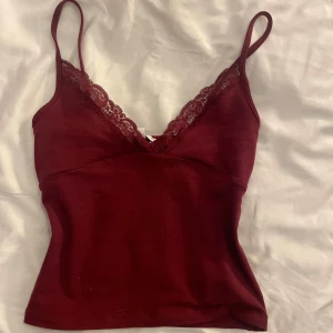 Vinröd linnetopp med spetskant - Supersnygg vinröd linnetopp med tunna axelband och v-ringning dekorerad med spets. Perfekt för lager på lager eller som statement-piece. Mjuk och stretchig känsla, sitter tajt och framhäver figuren. Är som ny skick har kvar lappen men råkade rycka av den för hastigt inte använd nån gång. Orgenalpris är ungefär 260