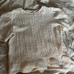 Vit blus med spetsdetaljer från Zara - Supersöt vit blus från Zara med kort puffärm och vackra spetsdetaljer på ärmar och nederkant. Blusen har en strukturerad, krinklad yta och rund halsringning. Perfekt för dig som gillar romantiska och unika plagg med extra detaljer.plus den har några fläckar som är lite synliga.