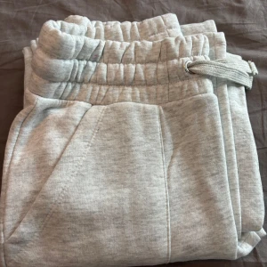 Ljusgrå mjukisbyxor från 157 - Mysiga ljusgrå mjukisbyxor från 157 med bred resår i midjan och dragsko. Byxorna har stora fickor fram och bak, raka ben och är gjorda i mjuk bomullsblandning. Helt oanvänd men där är ingen lapp kvar, storlek S