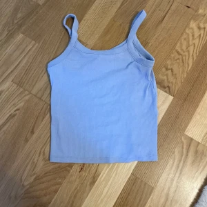 Ljusblå ribbad linnetopp från hm - Säljer en ljusblå ribbad linnetopp med smala axelband. Toppen är croppad och har en enkel, stilren design som passar perfekt till jeans eller kjol. Mjuk och stretchig för en bekväm passform. Den är stretchig.