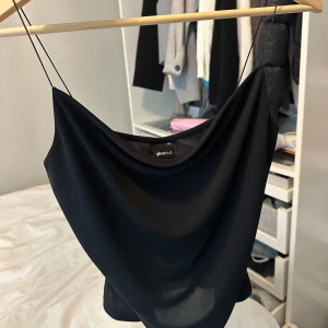 Svart linnetopp från Gina Tricot - Säljer en svart linnetopp från Gina Tricot med tunna axelband och snygg draperad urringning. Toppen har en stilren och enkel design som är lätt att matcha med jeans eller kjol. Perfekt för dig som gillar minimalistisk stil och vill ha något som känns både trendigt och klassiskt.