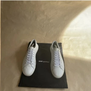Vita YSL sneakers - Säljer dessa vita ysl sneakers då jag köpt nya. De är inte i toppskick då sulan börjat lossna på yttersidorna, en del crease och allmänt slitage. Hör gärna av er vid frågor och funderingar, samt bilder på defekterna. Dustbag medföljer.
