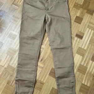 Beige skinny byxor från Vero Moda - Snygga beige byxor från Vero Moda i slim fit-modell. Byxorna har dragkedjor vid bensluten och klassisk femficksdesign. Tillverkade i mjuk bomullsblandning med stretch för extra komfort. Perfekta till sneakers eller boots.