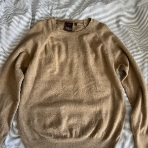 Beige tröja från Oscar Jacobson  - Snygg beige tröja från Oscar Jacobson i mjuk ull. Klassisk rund halsringning, ribbade muddar och diskret OJ-brodyr vid nederkanten. Perfekt för dig som gillar stilrena och lyxiga plagg med en clean vibe. 