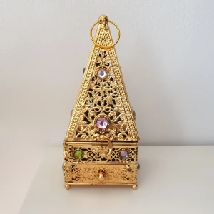 Guldig rökelsehållare med ädelstensdetaljer - En lyxig, pyramidformad rökelsehållare i guldfärgad metall med utskurna mönster och färgglada ädelstensliknande dekorationer. Boxen har ett handtag upptill och en utdragbar låda, perfekt för att förvara små sminkprodukter eller smycken.