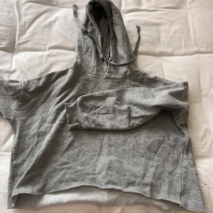  Croppad oversized hoodie  - Grå hoodie i croppad modell med rå kant nertill. Tröjan har huva med snörning och är fodrad med mjuk fleece på insidan. 