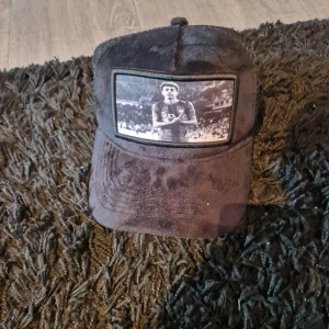 Svart keps från Evosportswear med tryck - Svart keps från Evosportswear med mjuk yta och ett stort svartvitt tryck framtill av en fotbollsspelare på arenan. Kepsen har böjd skärm och mesh på insidan för extra ventilation. Perfekt för dig som gillar sportig stil.