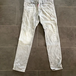 Ljusgrå slitna jeans från Dsquared2 - Säljer ett par ljusgrå jeans från Dsquared2 med slitningar och trasiga detaljer framtill och baktill. Klassisk femficksmodell med Dsquared2-logga bak i midjan. Jeansen har rak passform och är tillverkade i bomull.