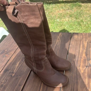 Bruna stövlar med klack och kontrastsöm - Snygga bruna stövlar i skinn med markerade vita sömmar och rund tå. Modellen har en stadig klack och platt sula framtill, perfekt för dig som gillar klassisk western-inspirerad stil. Passar till både jeans och klänning. Nypris 1899kr