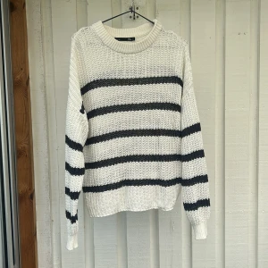 Randig stickad tröja i vitt och svart - Säljer en chunky stickad tröja i vitt med blåa horisontella ränder. Tröjan har rund halsringning, långa ärmar och en loose fit. Perfekt för lager-på-lager och chill vibes.