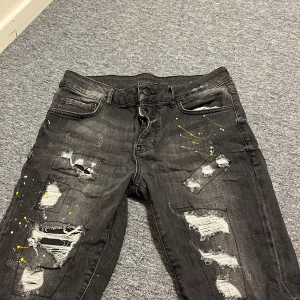 Svarta Dsquared2 jeans - Svarta slim fit jeans från Dsquared2 med coola slitningar, trasiga detaljer och färgstänk i gult och vitt. Jeansen har klassisk femficksdesign, knappgylf och en snygg tvättad look. Perfekta för dig som gillar streetstyle och vill sticka ut.