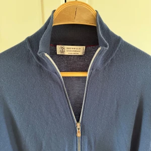 Brunello Cucinelli tröja  - Supersoft blå kofta i lyxig kashmir från Brunello Cucinelli. Modellen har hel dragkedja, ribbade muddar och hög krage. Perfekt för dig som gillar stilrena och exklusiva plagg med en chill vibe. Passar till allt och känns riktigt skön mot huden.