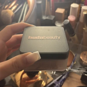 Huda Beauty löspuder - Löspuder från Huda Beauty i en snygg svart och transparent burk med roséguldfärgad logga. Perfekt för att fixera sminket och ge en matt finish. Kommer i en praktisk förpackning som är enkel att ta med i väskan. Som ny förpackning finns och kvitto