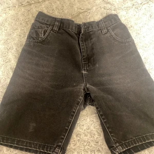 Svarta jeansshorts från Next - Svarta jeansshorts från Next med klassisk femficksdesign och bälteshällor. Modellen har raka ben och elastisk midja baktill för extra komfort. Tillverkade i 100% bomull och passar perfekt till sommaren. Snygg, enkel stil som funkar till allt.