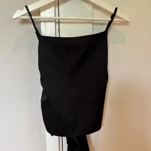 Svart linnetopp med knyt från Zara - Säljer en svart linnetopp från Zara i storlek XS. Toppen har smala axelband och en snygg knytning i ryggen, aldrig använd så är i helt nytt skick 