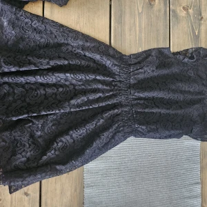 Svart spetsklänning med markerad midja - Supersnygg svart kortklänning i spets med markerad midja och rund hals. Klänningen har ett vackert mönster i spetsen och är perfekt för dig som gillar en klassisk men ändå cool stil. Passar dig som vill sticka ut lite extra!