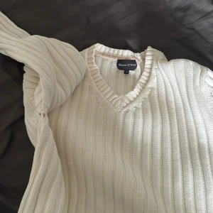 Vit ribbad tröja från Marc O'Polo - Säljer en stilren vit ribbad tröja från Marc O'Polo. Tröjan har en v-ringad hals och långa ärmar, perfekt för en avslappnad men snygg look. Passar bra till både jeans och chinos. Perfekt för kyligare dagar! Men har dock ett litet hål i höger armhåla men kan lätt sys ihop! 