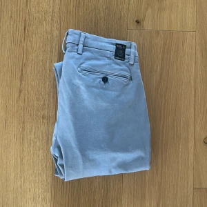 GRÅA CHINOS FRÅN REPLAY - Säljer ett par chinos från replay, färgen är grå. Perfekta nu inför vår/ sommar. Storleken är W29. Har en liten slitning på knäet som man knappt märker av. Skriv om ni har fler frågor och gå in och titta på profilen, säljer massa gamla plagg från garderoben.