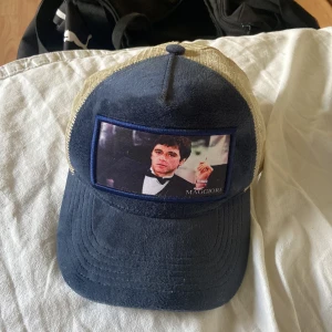 Blå och beige keps med tryck - Snygg keps i blått och beige med ett tryck på framsidan. Kepsen har ett nätmaterial på baksidan och justerbar rem för perfekt passform. Perfekt för en avslappnad stil.