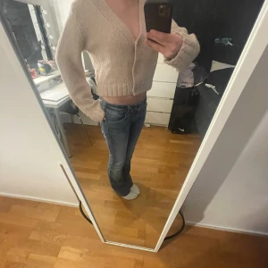 Rosa stickad kofta - Säljer en mysig rosa stickad kofta med v-ringning och långa ärmar. Koftan är croppad och har ribbade muddar vid ärmslut och nederkant. Perfekt för en avslappnad stil.