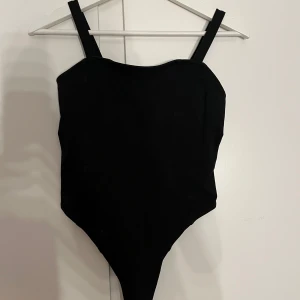 Svart bodysuit - Snygg svart bodysuit från H&M med breda axelband och knäppning i grenen. Perfekt för en stilren look.