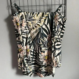 Blommig topp från Flash Woman - Säljer en somrig blommig topp från Flash Woman i storlek S. Toppen har smala axelband och ett tropiskt mönster med stora blommor och blad i gröna och vita nyanser. 