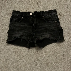 Svarta jeansshorts - Snygga svarta jeansshorts med fransiga kanter och klassisk femficksdesign. Perfekta för en avslappnad stil. De har en knapp och dragkedja framtill.