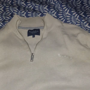 Beige tröja med dragkedja från Bondelid - Säljer en stilren beige tröja från Bondelid med dragkedja i halsen. Tröjan har en broderad logga på bröstet och är perfekt för en avslappnad look. Passar bra till både jeans och chinos.