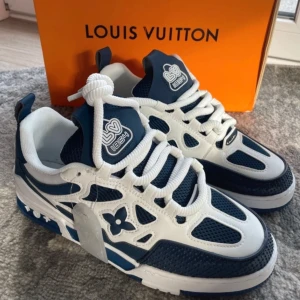 Lv skate - Snygga sneakers från Louis Vuitton i blått och vitt med märkets ikoniska blomma på sidan. Skorna har en rund tå och snörning, vilket ger en klassisk look. Perfekta för dig som vill ha stil och komfort i ett.