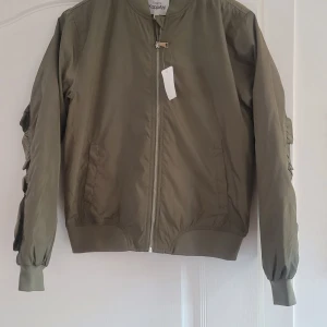 Olivgrön bomberjacka med volangdetaljer - Snygg olivgrön bomberjacka från KappAhl med volangdetaljer på ryggen