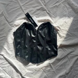Svart vegansk korsett - Snygg svart korsett i veganskt material från H&M Den är axelbandslös med en stilren design och dragkedja i ryggen. Perfekt för en trendig look.