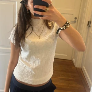 Vit ribbad topp - Säljer en stilren vit ribbad topp med korta ärmar. Perfekt för en avslappnad look. Toppen har en hög hals och en bekväm passform.