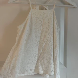 Vit spetslinne - Säljer en söt vit spetslinne med tunna axelband och knytning i ryggen. Perfekt för varma dagar eller som ett lager under en kavaj. Den har en luftig passform och vacker spetsdetalj som ger en romantisk känsla. Knappt använt den någon gång. 