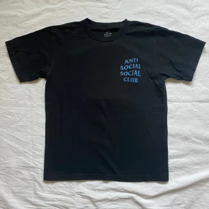 Svart t-shirt från Anti Social Social Club - Säljer en svart t-shirt från Anti Social Social Club med blå text på framsidan och ett färgglatt mönster på baksidan. 