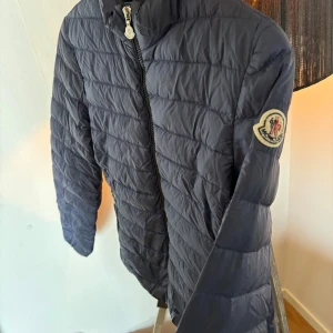 Moncler jacka  - Säljer en snygg mörkblå dunjacka från Moncler med dragkedja framtill och två praktiska fickor. Jackan har en quiltad design och Moncler-logga på ärmen. Perfekt för kyligare dagar! Äkta självklart, köptes på NK